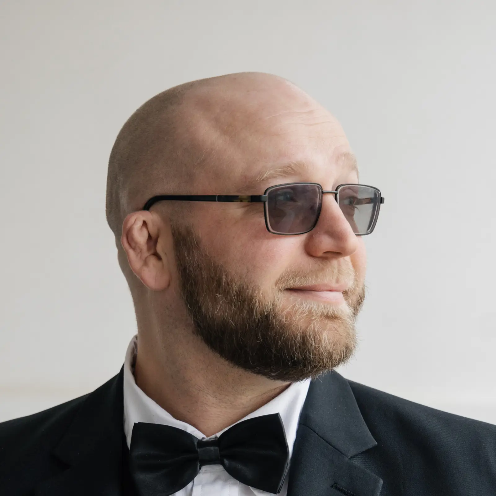 Joshua Mykitta in sunglasses and a tuxedo, looking to the right with a subtle, pensive smile